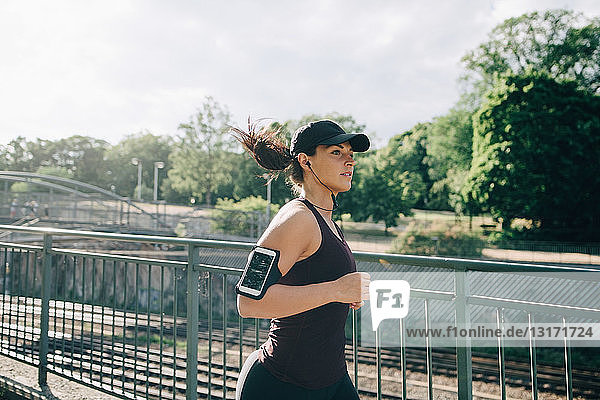 Selbstbewusste Sportlerin  die beim Joggen auf einer Brücke in der Stadt über In-Ear-Kopfhörer Musik hört