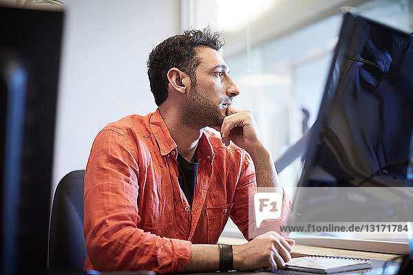 Thoughtful creative businessman sitting at computer desk in office
