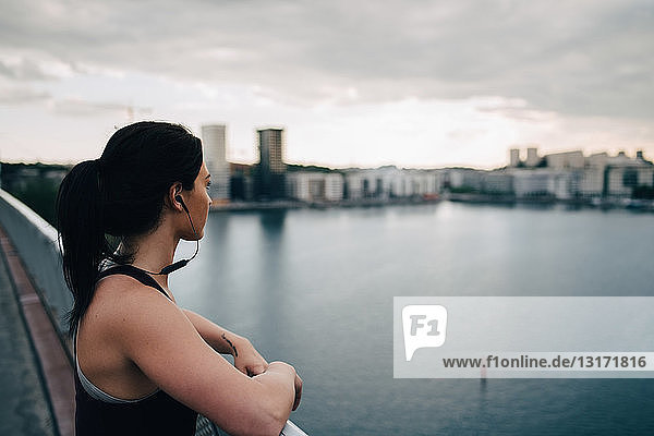 Side view of female athlete looking at city while standing on footbridge over sea