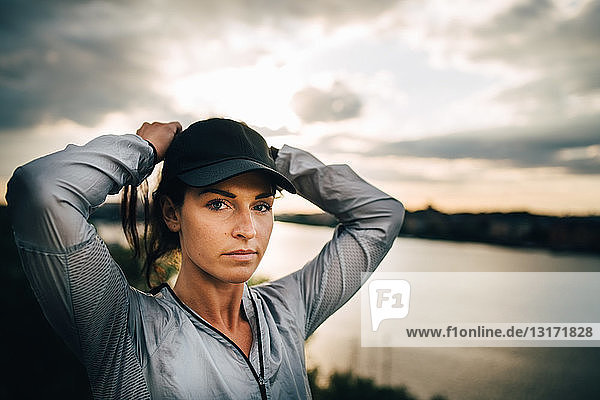 Porträt einer selbstbewussten Sportlerin  die sich bei Sonnenuntergang die Haare bindet  während sie auf einem Hügel steht