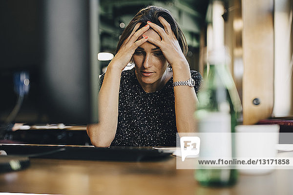 Frustrated female computer programmer with head in hands at office desk
