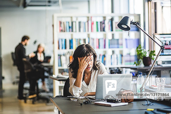 Müde Geschäftsfrau lehnt am Laptop auf dem Schreibtisch im Kreativbüro
