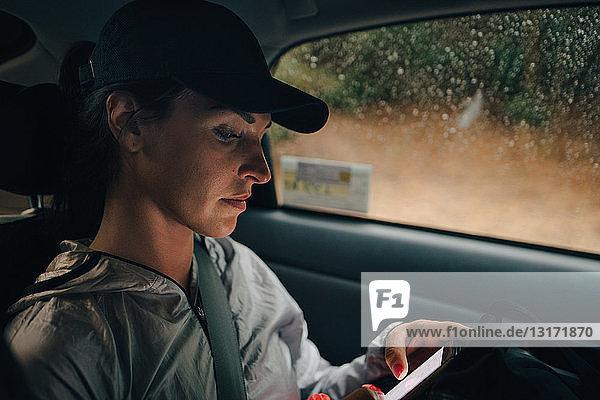 Sportlerin  die während der Regenzeit im Auto unterwegs ist und ein Mobiltelefon benutzt