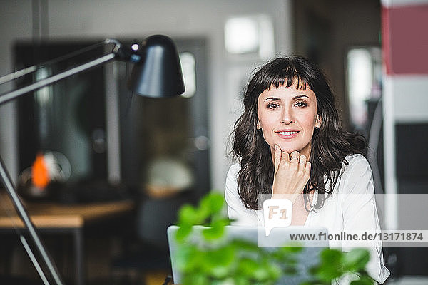 Porträt einer selbstbewussten Geschäftsfrau  die im Büro am Schreibtisch sitzt