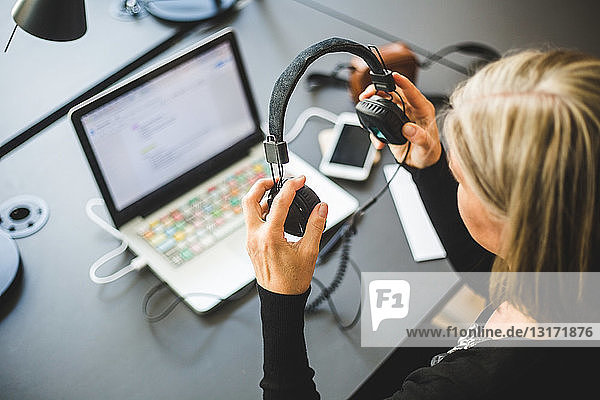 High angle view of businesswoman using headphones attached to laptop at desk in office