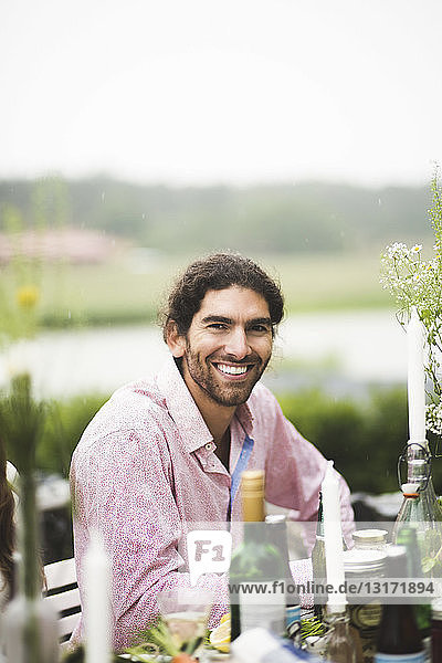 Portrait of smiling man sitting at dining table during dinner party in backyard