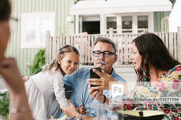 Mid adult woman showing mobile phone to family while sitting in backyard