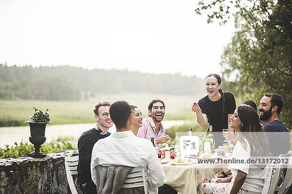 Cheerful male and female friends enjoying dinner party in backyard during weekend