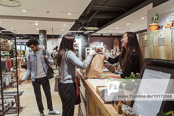 Smiling saleswoman giving merchandise to customer at checkout counter