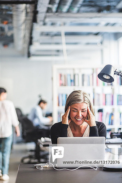 Geschäftsfrau lächelt  während sie im Büro auf den Laptop schaut