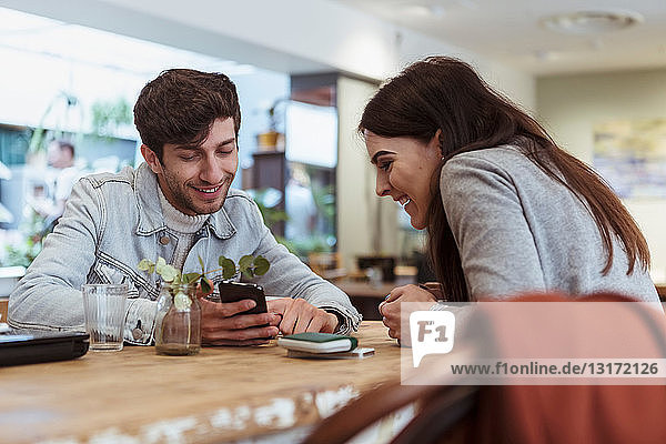 Lächelnde männliche und weibliche Freunde schauen auf das Smartphone im Cafe