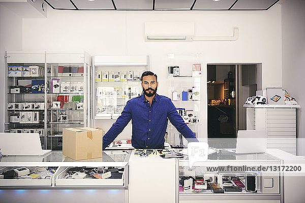 Portrait of confident owner standing at counter in electronics store