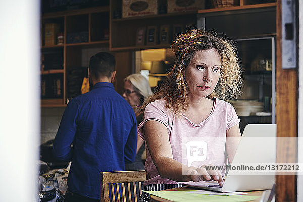 Reife Verkäuferin mit Laptop am Tisch im Feinkostladen