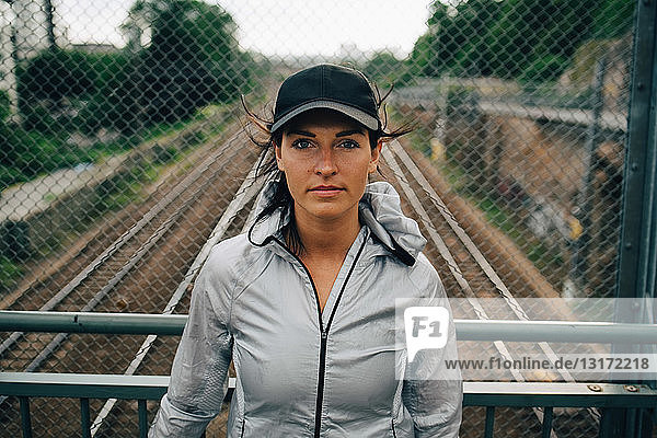 Porträt einer selbstbewussten Sportlerin  die auf der Brücke gegen das Geländer steht