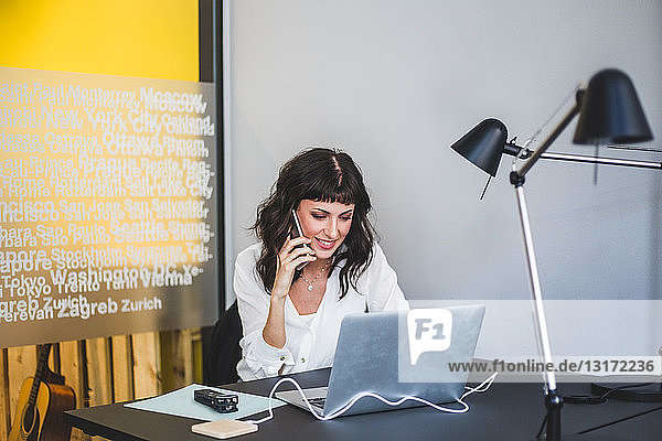 Geschäftsfrau lächelt beim Mobiltelefonieren am Schreibtisch im Kreativbüro