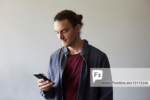 Creative businessman using smart phone against gray wall in office