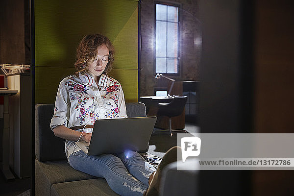 Junge Frau sitzt auf der Couch und arbeitet am Laptop