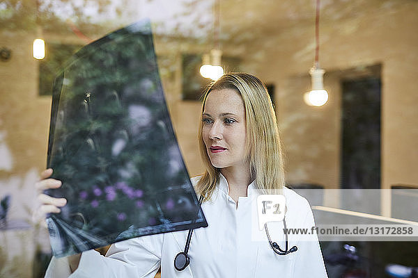 Ärztin schaut auf Röntgenbild hinter Fensterscheibe