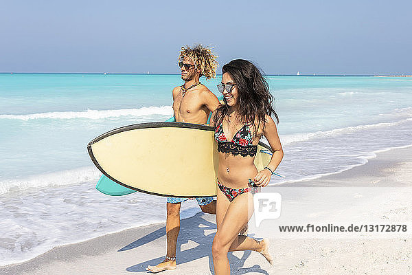 Couple running on the beach  carrying surfboards