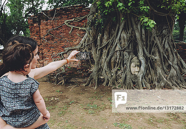 Thailand  Ayutthaya  Mutter und Tochter beim Fotografieren des Buddhakopfes zwischen Baumwurzeln im Wat Mahathat
