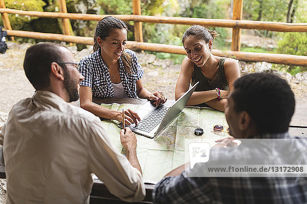 Group of hikers sitting together planning a hiking route using map and laptop