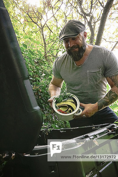 Reifer Mann wirft Küchenabfälle auf Komposthaufen ab