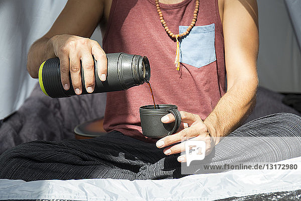Mann sitzt im Zelt und gießt Kaffee in eine Tasse  Teilansicht