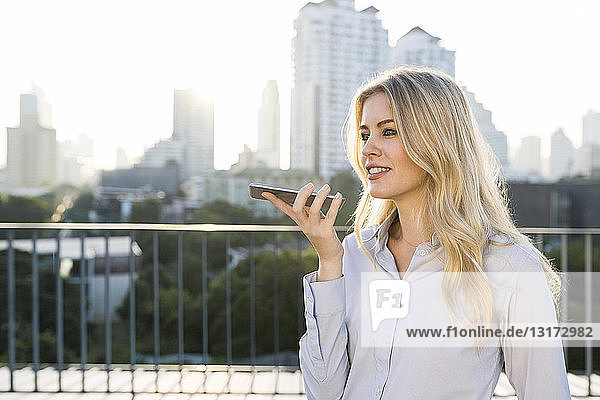 Blonde business woman speaking into smartphone on city rooftop