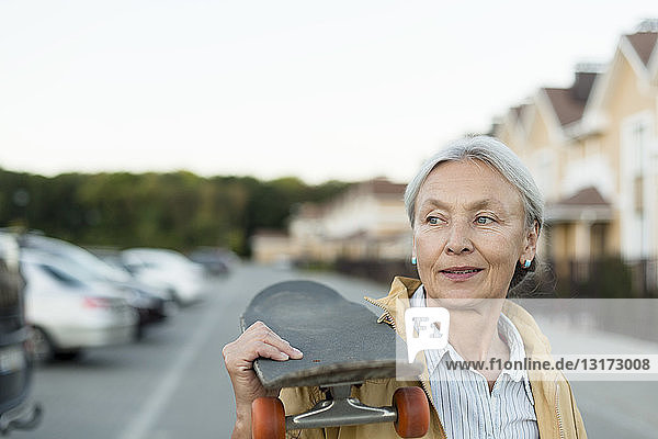 Porträt einer älteren Frau mit Skateboard auf der Schulter