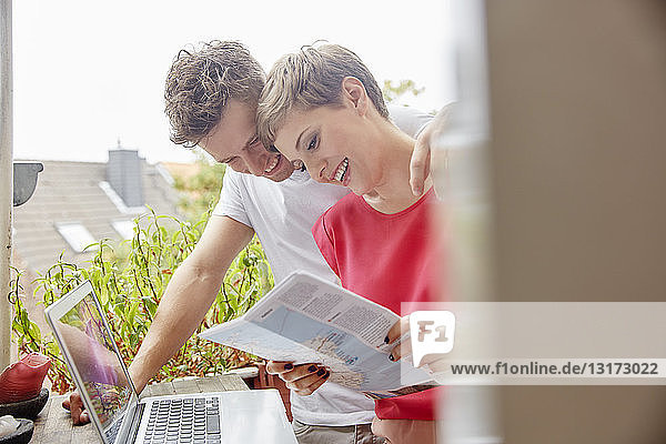 Glückliches Paar zu Hause auf dem Balkon mit Laptop und Karte