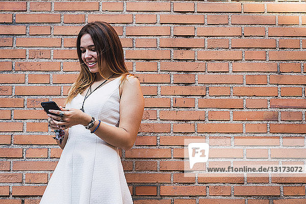 Laughing young woman in front of a brick wall using smartphone