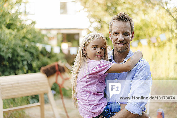 Portrait of smiling father carrying daughter in garden
