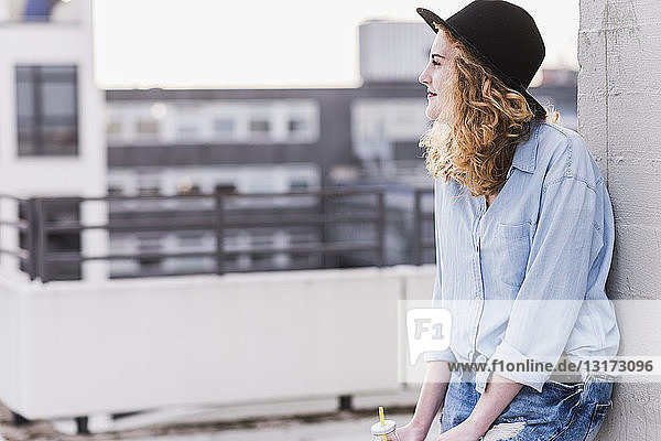 Zufriedene junge Frau mit Hut entspannt auf der Dachterrasse