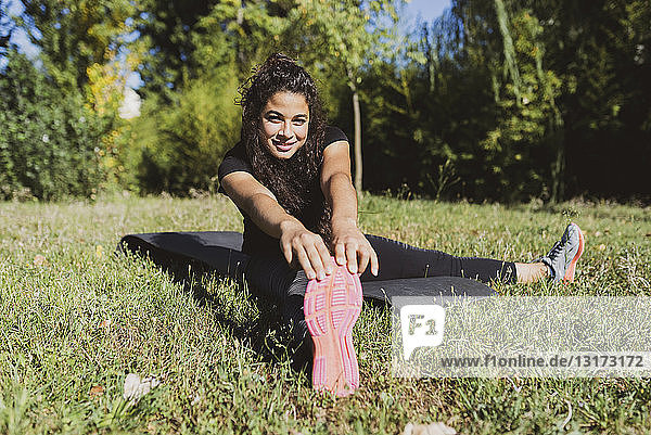 Sporty young woman stretching her leg on a meadow