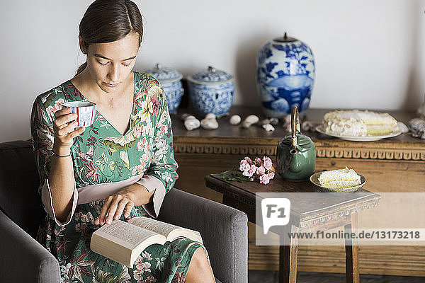 Young woman drinking cup of tea while reading a book at home