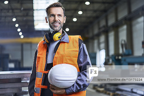 Porträt eines lächelnden Mannes mit Arbeitsschutzkleidung in der Fabrik