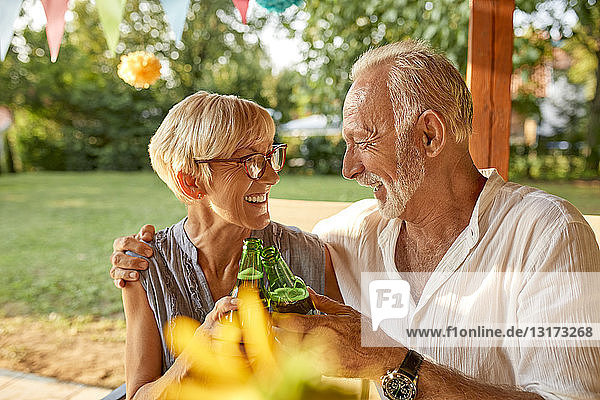Glückliches älteres Paar  das auf einer Gartenparty mit Bierflaschen klimpert