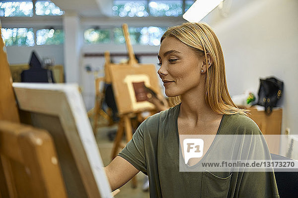 Lächelnde Schülerin malt im Kunstunterricht an der Staffelei