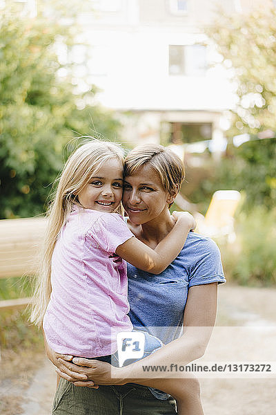 Portrait of smiling mother carrying daughter in garden