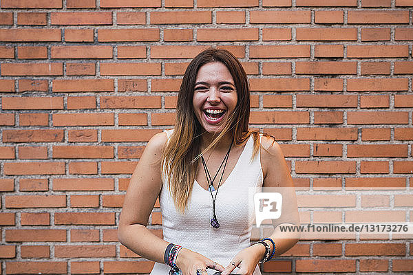 Porträt einer lachenden jungen Frau  die vor einer Ziegelmauer steht