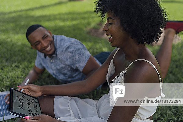 Glückliche junge Frau mit Freund in einem Park mit Tablette