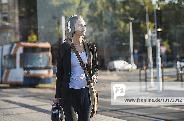 Young woman with headphones and cell phone at tram station