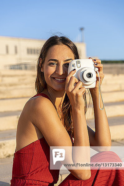 Porträt einer lächelnden jungen Frau  die ein Sofortfoto im Freien macht