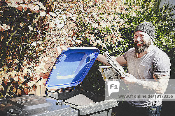 Porträt eines lachenden Mannes beim Recycling von Altpapier in einer Papierbank