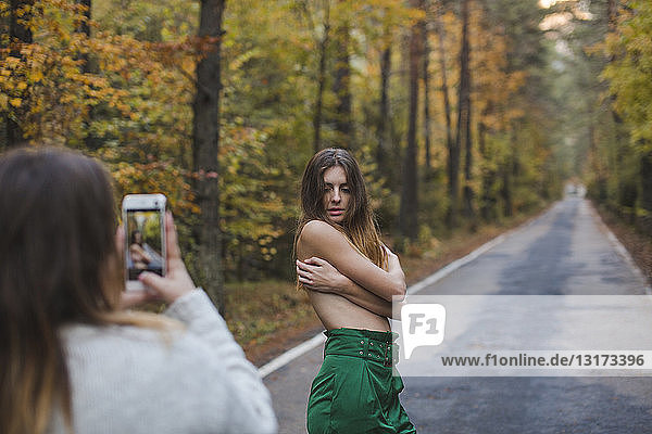 Frau macht Handy-Foto von barbusiger junger Frau  die auf einer Landstraße steht