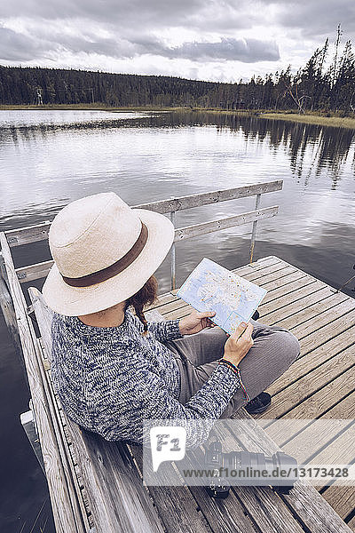 Schweden  Lappland  Mann mit Kamera sitzt auf einer Bank an einem Steg und schaut auf die Karte