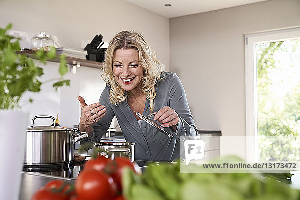 Lächelnde Frau kocht in der Küche und riecht am Kochtopf