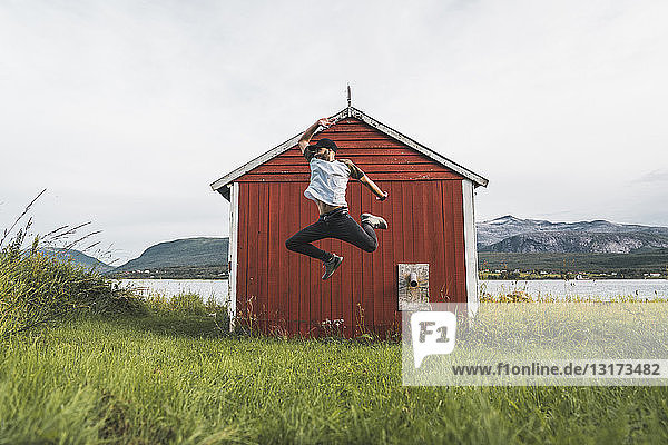 Junger Mann springt vor rote Scheune in Nordnorwegen