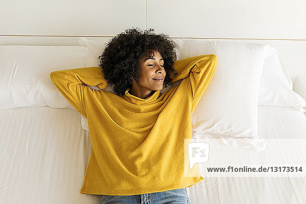 Lächelnde Frau mit geschlossenen Augen auf dem Bett liegend