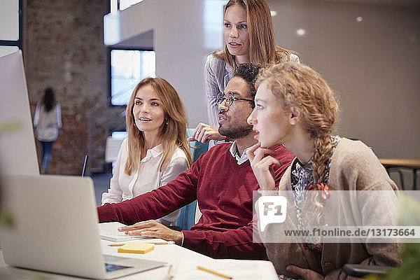 Colleagues looking over shoulder of young man working in modern office